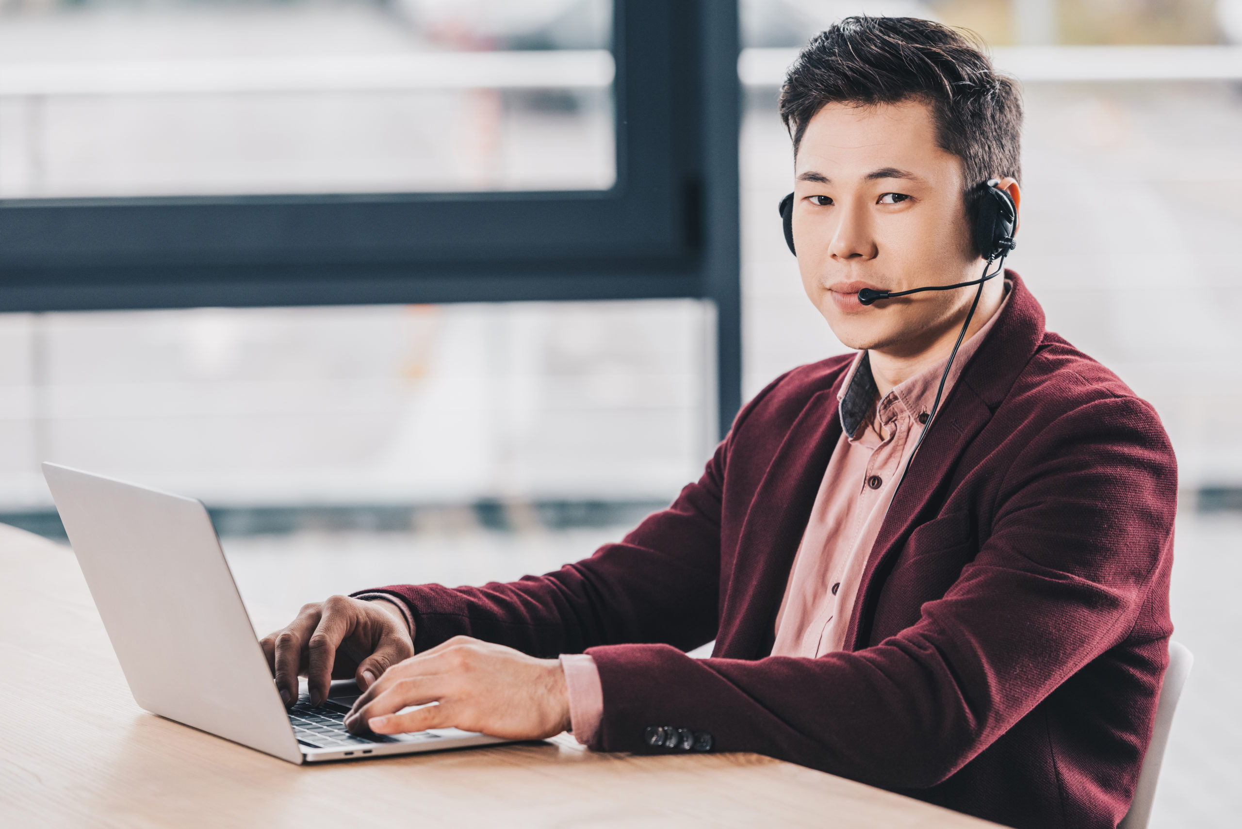 Handsome,Young,Kazakh,Businessman,In,Headset,Using,Laptop,And,Looking Male professional with headset works at laptop