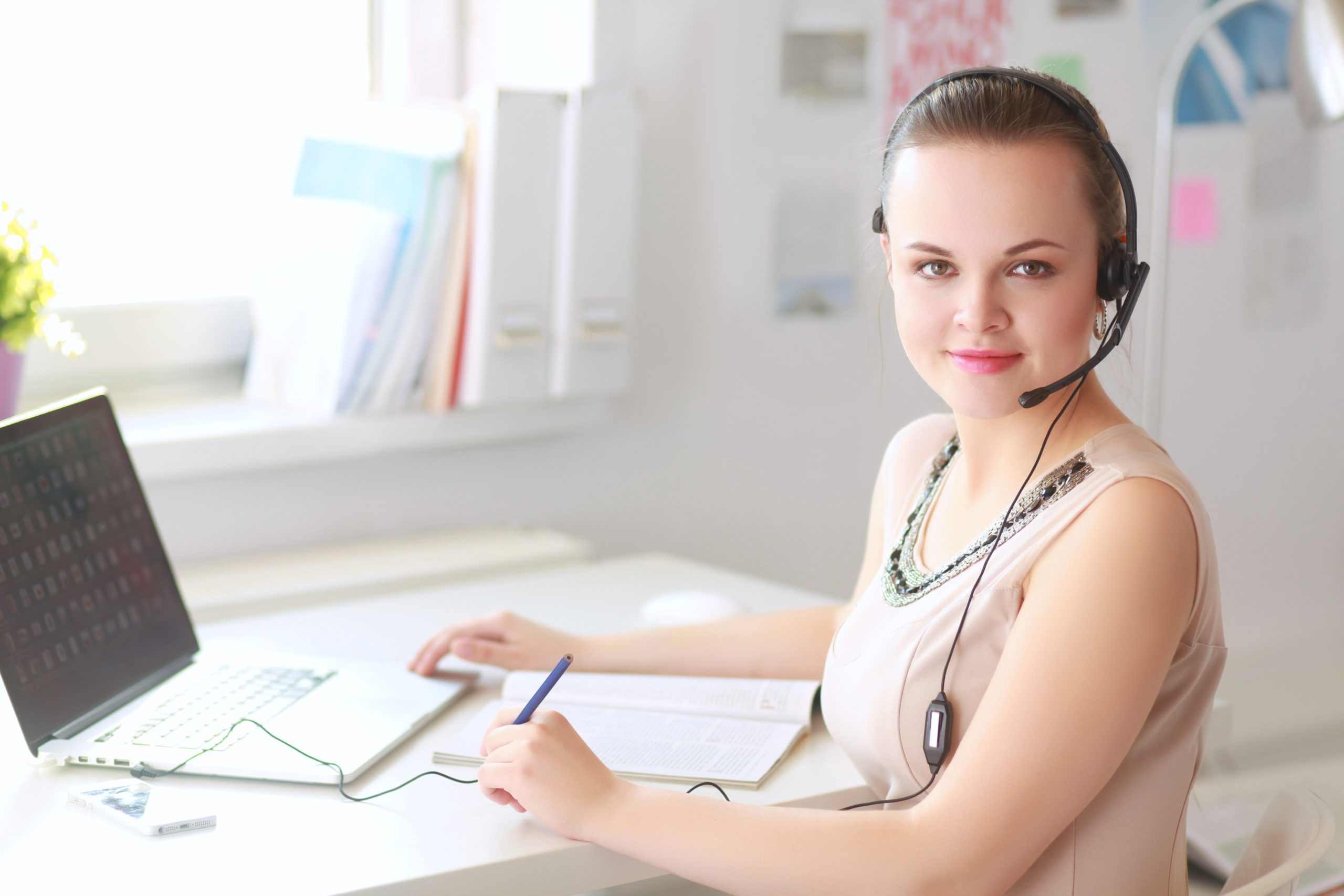 Businesswoman,Talking,On,The,Phone,While,Working,On,Her,Computer Female in professional beige dress wearing headset